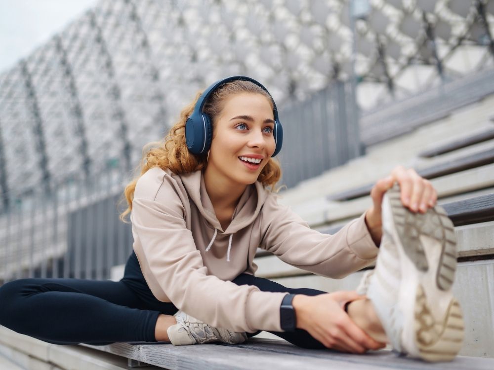 Woman stretching on a bench wearing headphones and a light-colored hoodie.