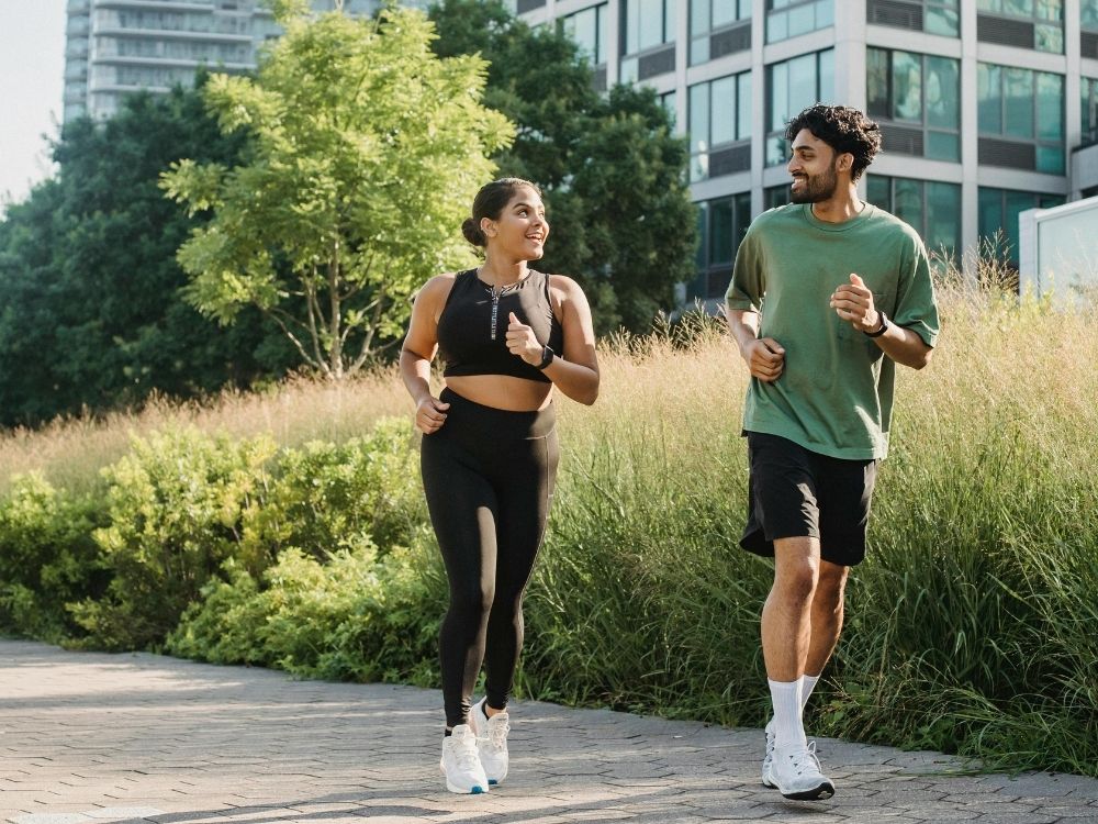 Two people jogging outdoors with buildings and greenery in the background